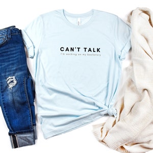May include: A light blue t-shirt with the text "CAN'T TALK I'm working on my backstory" printed in black.