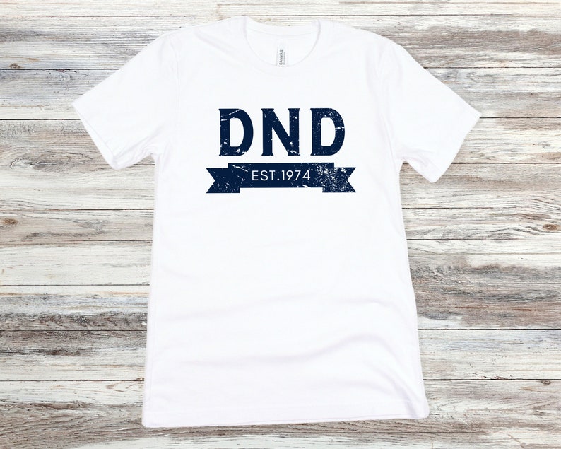 May include: White t-shirt with a blue graphic that says "DND EST. 1974" in a vintage style.