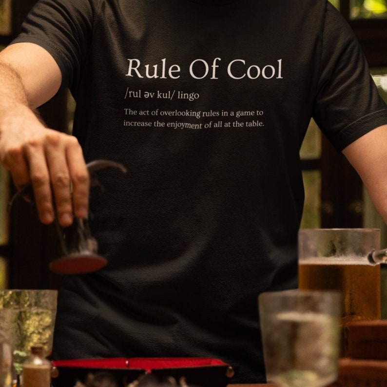 A Dungeon Master Playing Dungeons and dragons wearing a graphic tee with The Rule Of Cool - Definition on it.