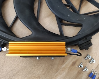 May include: A gold-colored heatsink with blue wire connectors and a black fan in the background. There are also some screws and nuts on a wooden surface.