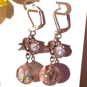 May include: Silver tone earrings with a seashell and starfish charm hanging from a clear glass orb filled with iridescent glitter and seashells.