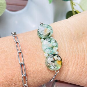 May include: A silver chain bracelet with a green and white beaded charm bracelet featuring seashells and pearls.