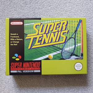 May include: A Super Nintendo Entertainment System video game box for Super Tennis. The lime green box features a tennis racket, a ball, and a net. Text includes 'Smash a Forehand, Rifle a Return, or Charge the Net!' and the Nintendo Seal of Quality.