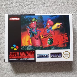 May include: A Super Nintendo Entertainment System game cartridge box for Worms, a video game featuring two red worms with guns and a bomb. The box is white with red, blue, and yellow accents. The game is licensed by Nintendo and published by Ocean.