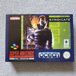 May include: A rectangular Super Nintendo Entertainment System video game box for the title Syndicate. The box features a dark blue and green colour scheme with an illustration of a character in a black jacket, the Ocean logo, and the Nintendo seal.