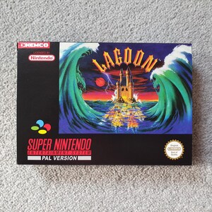 May include: A Super Nintendo game box for "Lagoon." The box features a vibrant illustration of a castle on an island, surrounded by large waves. The game title is in gold lettering. The box is black with the Nintendo and Kemco logos.