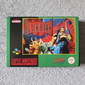 May include: A rectangular Super Nintendo Entertainment System game box for Blackhawk. The green and black packaging features the title in bold black letters, a central illustration of a muscular character with a pistol, and the Nintendo logo.