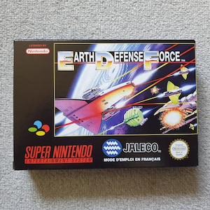 May include: A rectangular Super Nintendo Entertainment System video game box for Earth Defense Force by Jaleco. The black box features a space battle illustration with a spaceship, lasers, and planets. It includes the Nintendo logo and seal.