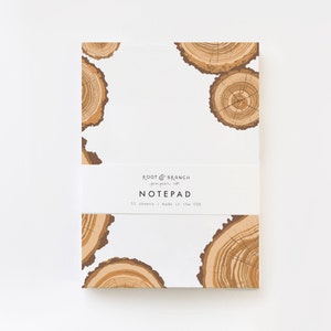 May include: A white notepad with a brown tree ring pattern. The notepad has a label that reads "Root & Branch paper co. NOTE PAD 50 sheets | made in the USA."