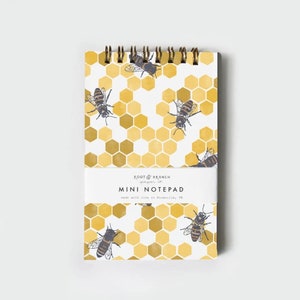 May include: A mini notepad with a spiral binding. The cover features a honeycomb pattern with bees. The notepad has the text "ROOT & BRANCH paper co." and "MINI NOTEPAD" with the text "made with love in Knoxville, TN".