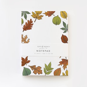May include: A notepad with a white background and a border of colorful fall leaves. The notepad has the text "Root & Branch paper co. NOTE PAD 50 sheets | made in the USA" printed on the front.