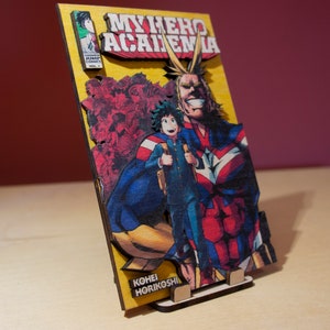 May include: Wooden My Hero Academia artwork featuring Deku and All Might. The artwork has a yellow background with the title "My Hero Academia" in red and white. The artist's name, Kohei Horikoshi, is also visible.