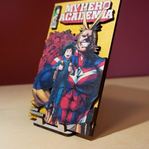May include: Wooden artwork featuring a vibrant illustration from "My Hero Academia." The image showcases All Might and Deku, with the series title prominently displayed. The artwork is mounted on a wooden base, creating a 3D effect.