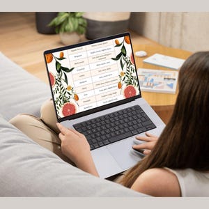 May include: A laptop displaying a fragrance notes chart with fruit illustrations. The screen shows a table with scent descriptions, including "Aquatic Accord," "Bergamot," and "Blackcurrant." The laptop is on a person's lap, with a keyboard visible.