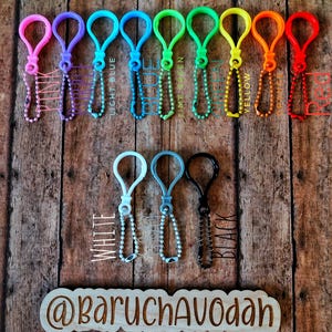 May include: A collection of colorful plastic keychains with metal ball chain attachments. The keychains are in various colors, including pink, purple, light blue, green, yellow, orange, and red. The text "LIGHT BLUE", "LIME GREEN", and "YELLOW" are visible. The bottom row includes white, light blue, and black keychains.