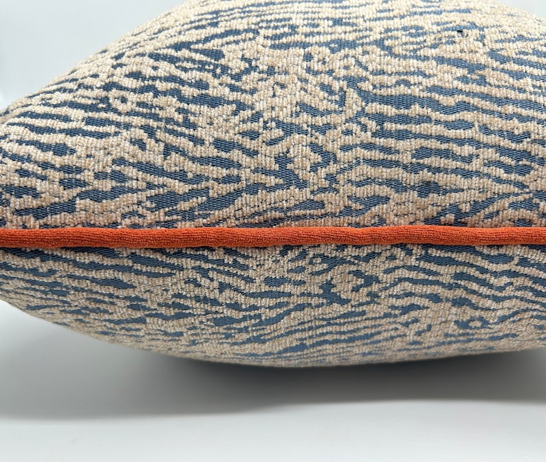 May include: A blue and beige patterned throw pillow with an orange trim. The pillow has a soft, textured fabric.