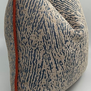 May include: A beige and blue patterned throw pillow with an orange trim. The pillow is made of a soft, textured fabric.