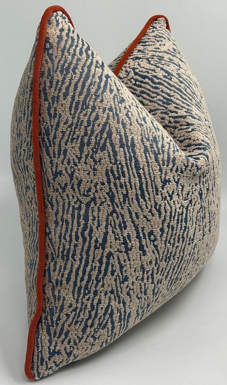 May include: A beige and blue patterned throw pillow with an orange trim. The pillow is made of a soft, textured fabric.