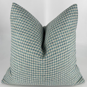 May include: A teal and white patterned throw pillow with a square shape. The pillow is made of a soft, textured fabric.