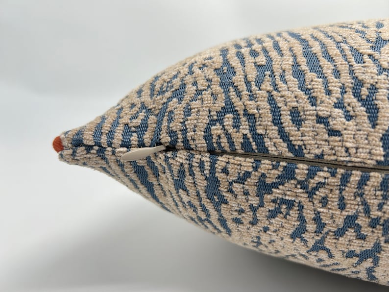 May include: Close-up of a blue and beige patterned throw pillow with a zipper closure.
