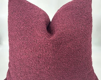 Può includere: Un cuscino decorativo quadrato di colore bordeaux intenso, con una superficie strutturata e a rilievo. Il cuscino appare morbido e confortevole, perfetto per aggiungere un tocco di colore e consistenza a un soggiorno o una camera da letto.