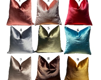 Op de afbeelding: Negen fluwelen kussenhoezen in verschillende kleuren, waaronder stoffig roze, blush roze, rood, blauwgrijs, olijfgroen, turquoise, beige, bruin en goud. Elke kussenhoes heeft een eenvoudig, elegant ontwerp met een puntige bovenkant en een naad in het midden.