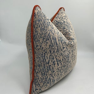 May include: A blue and beige patterned throw pillow with an orange trim. The pillow is made of a soft, textured fabric.