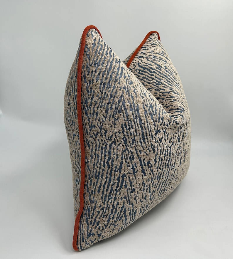 May include: A blue and beige patterned throw pillow with an orange trim. The pillow is made of a soft, textured fabric.