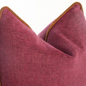 Op de afbeelding: Een bordeauxrood kussen met een bruine bies. Het kussen is gemaakt van een textuurstof.