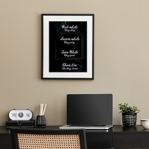 May include: A black framed print with the text "Work while they sleep, Learn while they party, Save while they spend, Then live like they dream." is displayed above a desk with a laptop, a small potted plant, and a black chair.
