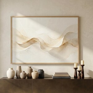 May include: A large framed abstract watercolor painting in neutral tones hangs above a dark brown cabinet. Various ceramic vases in beige and gray tones are arranged on top of the cabinet, along with books and wooden candle holders.