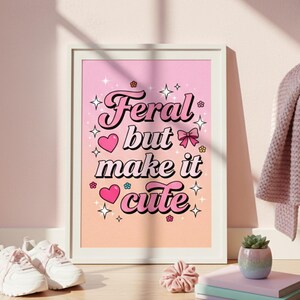 Puede incluir: Una impresi&oacute;n art&iacute;stica enmarcada con el texto "Feral but make it cute" en una fuente retro. La impresi&oacute;n tiene un fondo degradado rosa y melocot&oacute;n con corazones, estrellas y flores. La obra de arte se exhibe cerca de zapatillas blancas.