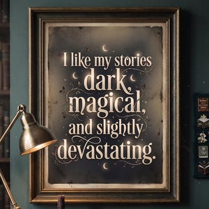 Op de afbeelding: Een ingelijste print met de tekst "I like my stories dark, magical, and slightly devastating." De tekst is wit op een donkere achtergrond, met een goudkleurige lijst. De afbeelding toont een bureaulamp en boeken.