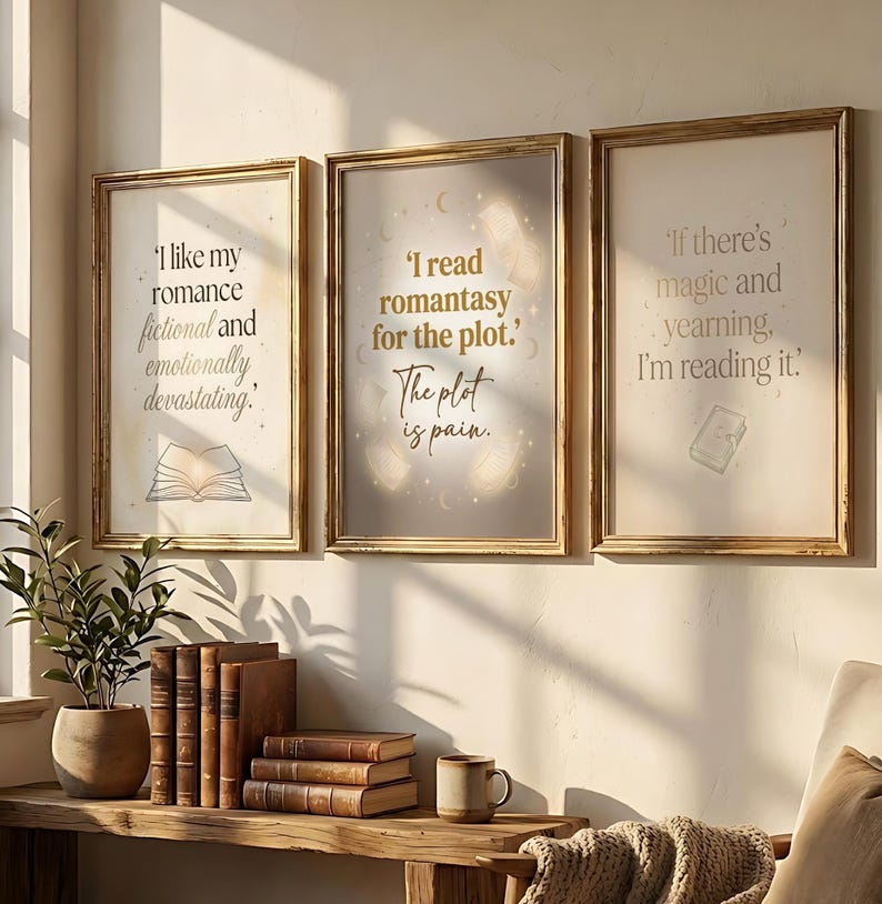 May include: Three framed art prints with gold frames and quotes about reading. The prints feature text like "I like my romance fictional and emotionally devastating" and "I read romantasy for the plot." A wooden shelf below holds books and a mug.