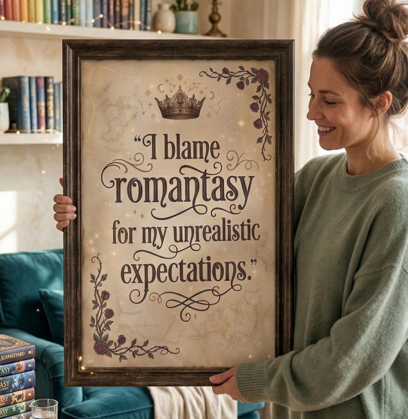 May include: A framed print with the text "I blame Romantasy for my unrealistic expectations." The print has a vintage parchment background, a gold crown, and floral accents. The frame is dark brown.