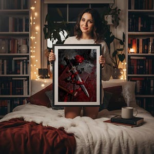 Puede incluir: Una obra de arte enmarcada con una rosa roja, una daga y un libro. La obra tiene un tema g&oacute;tico oscuro con tonos rojos y grises. El marco es negro.