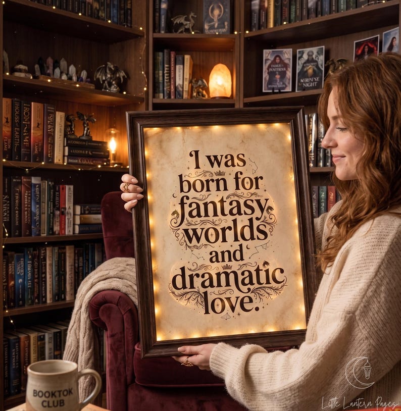 May include: A rectangular dark wood frame containing a parchment-colored sign with the black text: I was born for fantasy worlds and dramatic love. The sign is illuminated by a string of small warm white LED lights lining the inner frame edge.