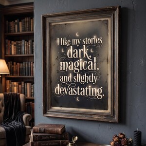 Op de afbeelding: Een ingelijste print met de tekst "I like my stories dark, magical, and slightly devastating." De print heeft een donkere achtergrond met witte letters en een decoratieve rand. De lijst is donkerbruin van kleur. De print hangt aan een donkerblauwe muur.
