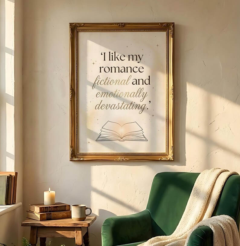 May include: A framed print with the quote, "I like my romance fictional and emotionally devastating." The print is in a gold ornate frame, with an illustration of an open book. The print hangs above a green armchair.