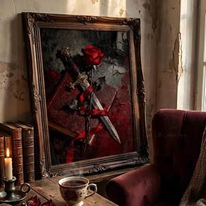 Puede incluir: Una obra de arte enmarcada con una rosa roja, una espada y un libro, todo entrelazado con una cinta roja. La obra de arte es de estilo oscuro y g&oacute;tico, con un marco de madera vintage. Una taza de t&eacute; y libros est&aacute;n sobre una mesa de madera.