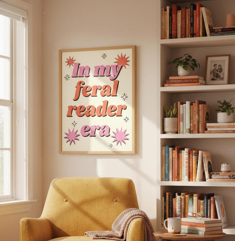 May include: A framed poster with the text "In my feral reader era" in pink and orange lettering. The poster is surrounded by starburst and star graphics. The poster hangs on a wall above a yellow armchair.