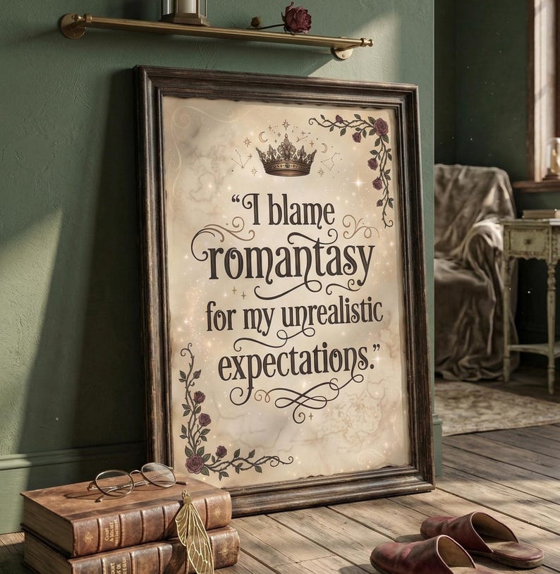 May include: Framed print with the quote "I blame romantasy for my unrealistic expectations." The print has a vintage map background, a crown, and floral accents. The frame is dark brown. The print is leaning against a green wall.