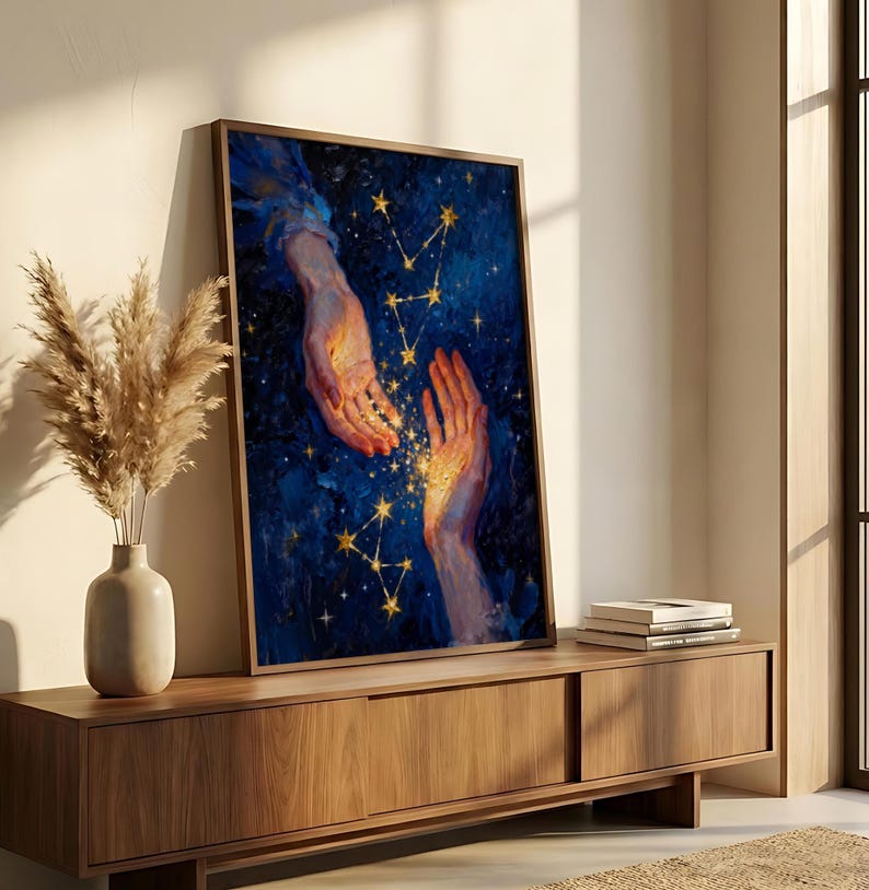 May include: A framed art print featuring a celestial theme. The artwork depicts two hands reaching towards each other against a dark blue background with golden stars and constellations. The hands are illuminated with a warm, golden light.