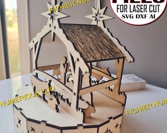 May include: A wooden nativity scene with a star on top, a manger with a baby Jesus inside, and a donkey and cow. The scene is on a round base with stars cut out. The text "FICHIER NUMERIQUE DIGITAL FILES FOR LASER CUT SVG DXF AI" is on the top of the image.
