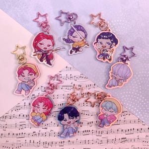 May include: A collection of character keychains with star-shaped clasps. Each keychain features a different anime-style character in various poses and outfits. The keychains are in shades of pink, purple, blue, and yellow.