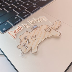 Może przedstawiać: Przezroczysta naklejka z kreskówkowym kotem i tekstem "Death by Debugging". Kot jest jasnobrązowy z białym brzuchem i ma robaka na grzbiecie. Tekst jest brązowym fontem.