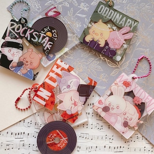 May include: A selection of clear acrylic keychains with cartoon animal designs. Each keychain features a different design, including a record, the word "ROCKSTAR", and the word "ORDINARY". The keychains have metal chain attachments.