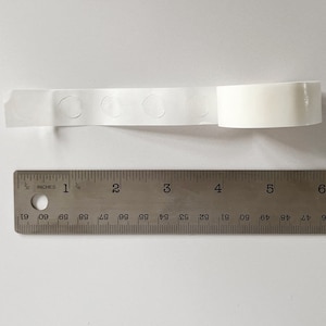 Detail of transparent glue dots roll unrolled. Each dot is double-sided and .47" round. 100 glue stickers per roll.