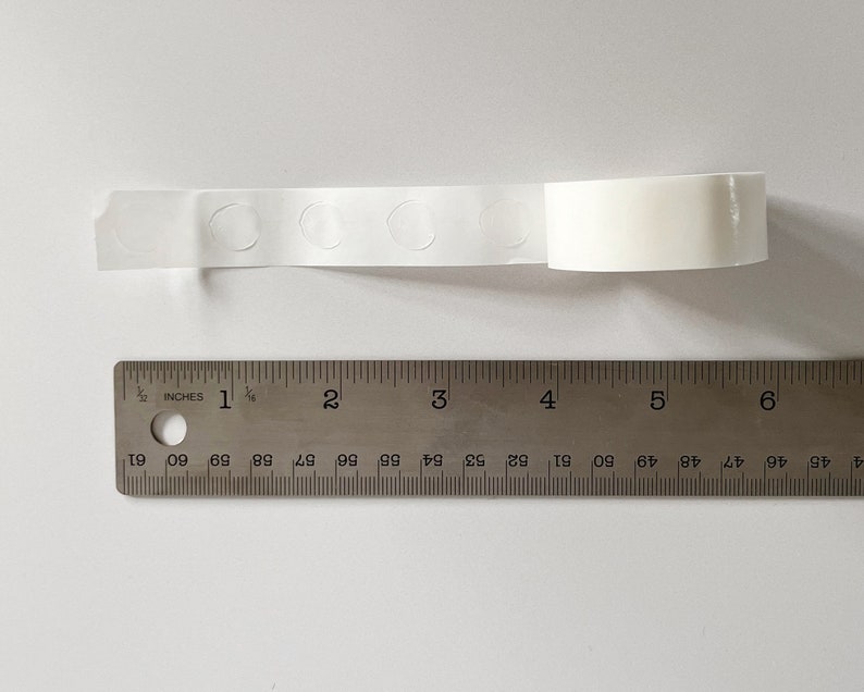 Detail of transparent glue dots roll unrolled. Each dot is double-sided and .47" round. 100 glue stickers per roll.