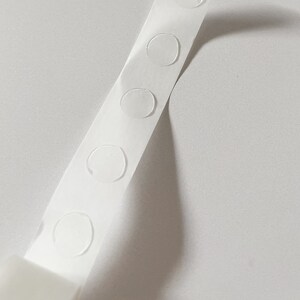Detail of transparent glue dots roll unrolled. Each dot is double-sided and .47" round. 100 glue stickers per roll.